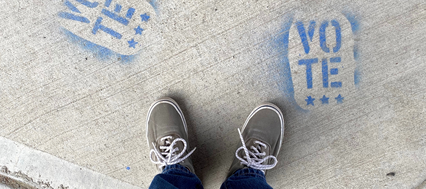 Person standing over vote stenciled on sidewalk